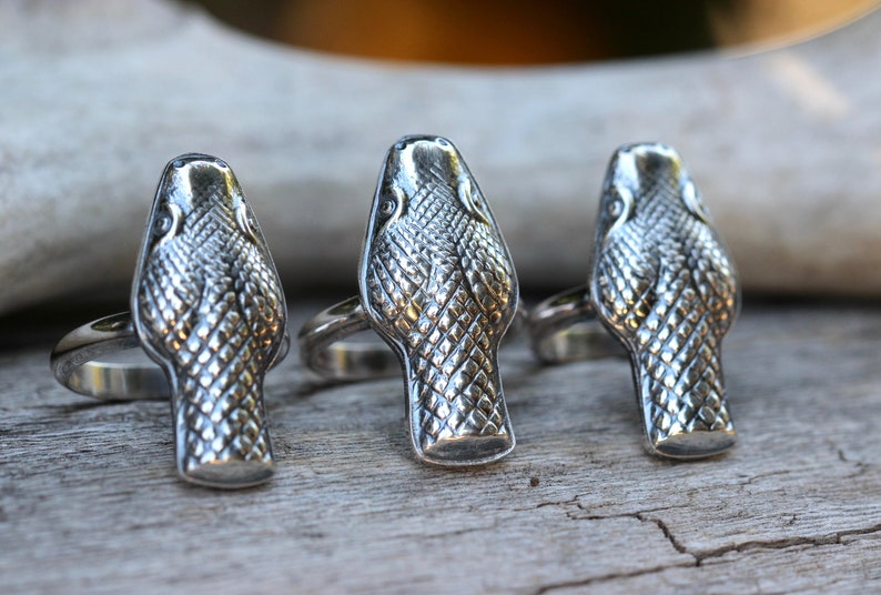 May include: Three silver snake head rings. The rings are detailed with scales and have a realistic snake head design.