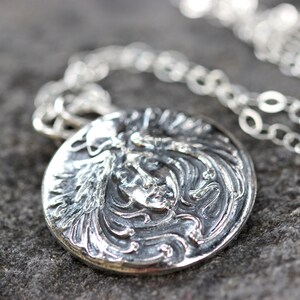 May include: A silver necklace with a round pendant featuring a detailed, embossed design of a woman's face with flowing hair.
