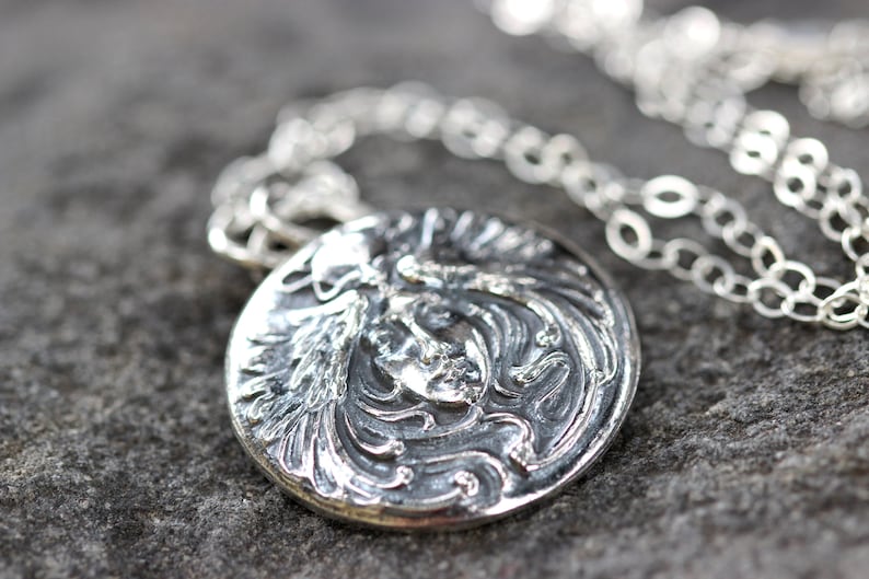 May include: A silver necklace with a round pendant featuring a detailed, embossed design of a woman's face with flowing hair.