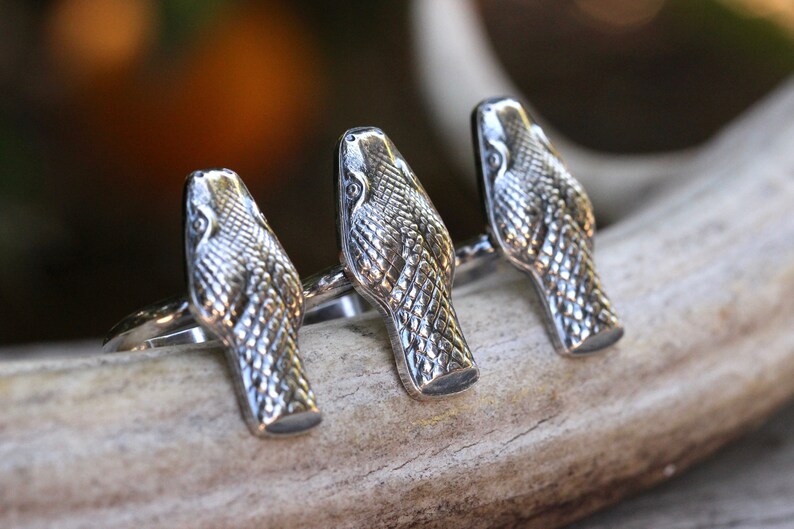 May include: Three silver snake head rings. The rings are stacked on top of each other and are made of a detailed snake head design.