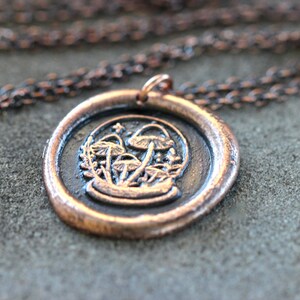 May include: A copper necklace with a wax seal pendant featuring a cluster of mushrooms in a circular design.