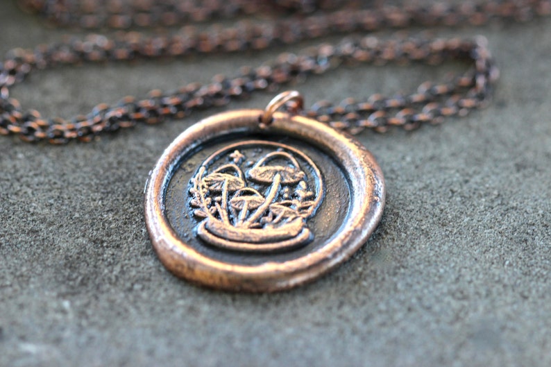May include: A copper necklace with a wax seal pendant featuring a cluster of mushrooms in a circular design.