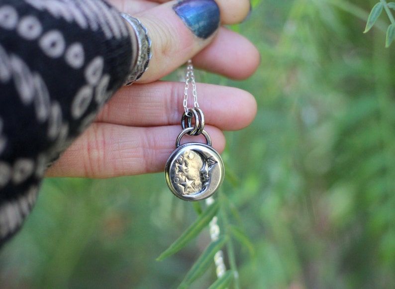 Puede incluir: Un collar de plata con un dije de luna creciente con un dise&ntilde;o de estrella. El dije cuelga de una cadena de plata.