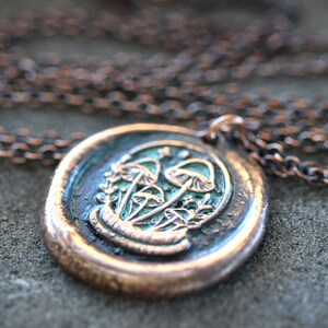 May include: A copper chain necklace with a round pendant featuring a detailed design of mushrooms in green and white.