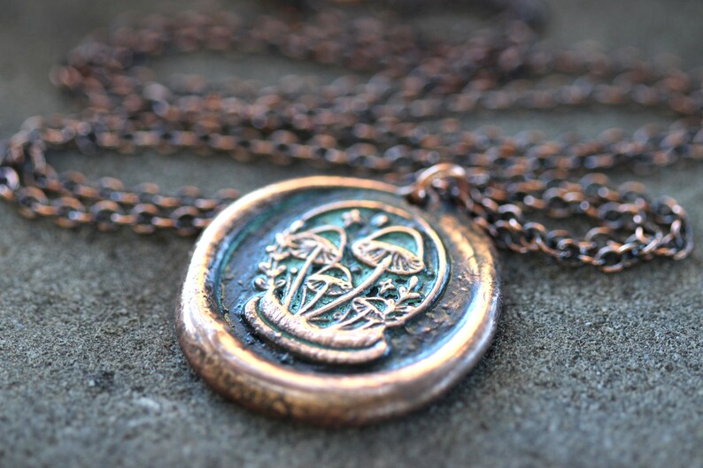 May include: A copper chain necklace with a round pendant featuring a detailed design of mushrooms in green and white.