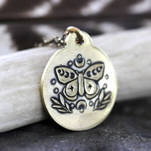 Peut inclure: Un collier avec un pendentif en laiton repr&eacute;sentant un papillon grav&eacute; avec des croissants de lune et des &eacute;toiles. Le pendentif est rond et suspendu &agrave; une cha&icirc;ne d&eacute;licate.