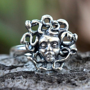 Puede incluir: Un anillo de plata con un dise&ntilde;o detallado de la cabeza de Medusa rodeada de serpientes.