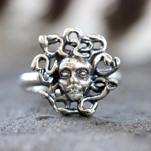 Puede incluir: Un anillo de plata con una escultura detallada de la cabeza de Medusa con serpientes como cabello.
