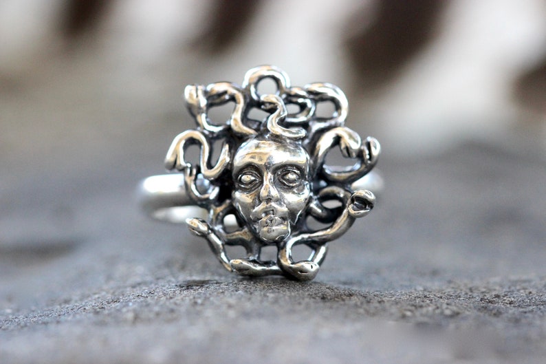 Puede incluir: Un anillo de plata con una escultura detallada de la cabeza de Medusa con serpientes como cabello.