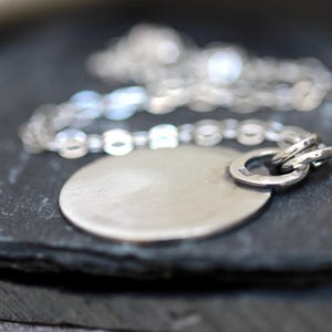 May include: A silver necklace with a round pendant. The pendant is smooth and has a shiny finish. The chain is delicate and has a simple design.