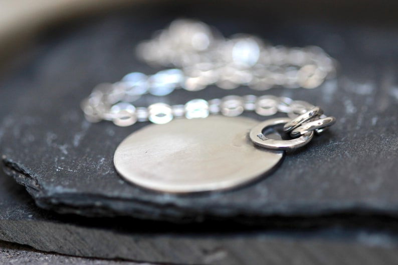 May include: A silver necklace with a round pendant. The pendant is smooth and has a shiny finish. The chain is delicate and has a simple design.