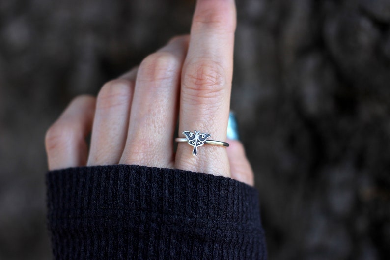 May include: A silver ring with a delicate butterfly design. The ring is worn on a finger and the butterfly is facing the viewer.