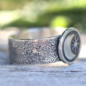 May include: A silver ring with a textured band and a crescent moon and star design.