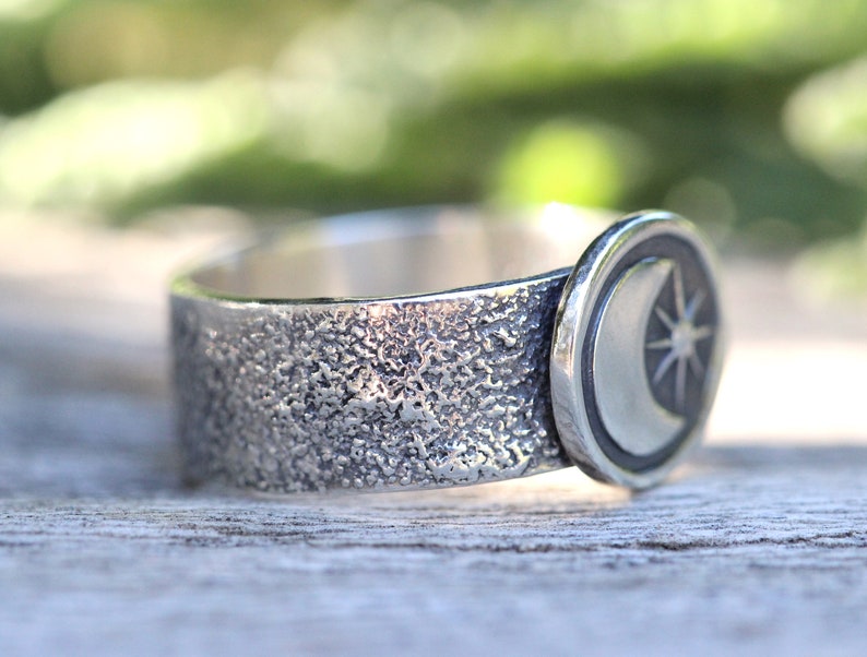 May include: A silver ring with a textured band and a crescent moon and star design.