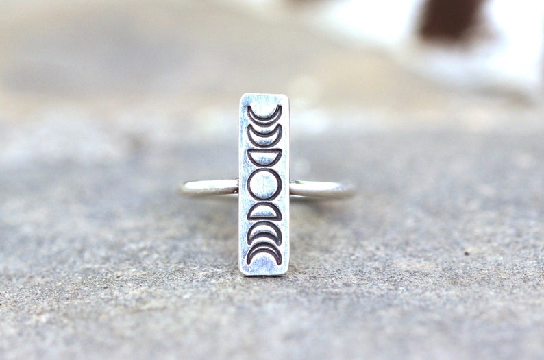 May include: A silver ring with a rectangular band featuring a design of eight crescent moons in different phases.