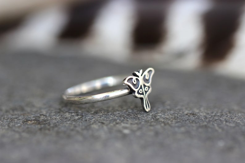 May include: A silver ring with a detailed butterfly design. The butterfly is facing to the right and has a black outline.