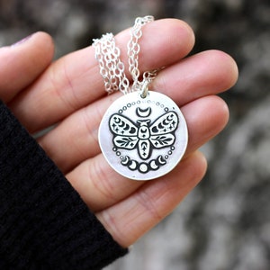 May include: A silver necklace with a round pendant featuring a detailed etched design of a moth with crescent moons and stars.