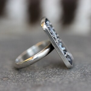 May include: A silver ring with a rectangular, textured design. The ring is made of sterling silver and has a polished finish.