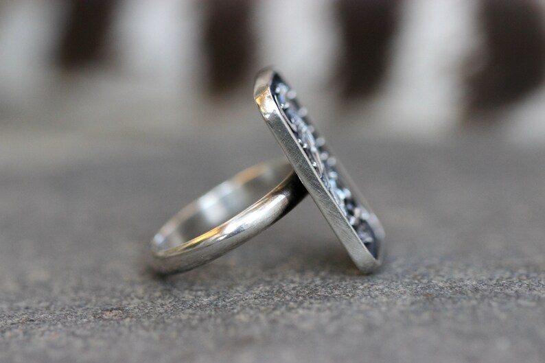 May include: A silver ring with a rectangular, textured design. The ring is made of sterling silver and has a polished finish.