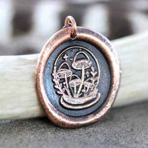 May include: A copper pendant with a black wax seal featuring a detailed illustration of mushrooms and foliage.