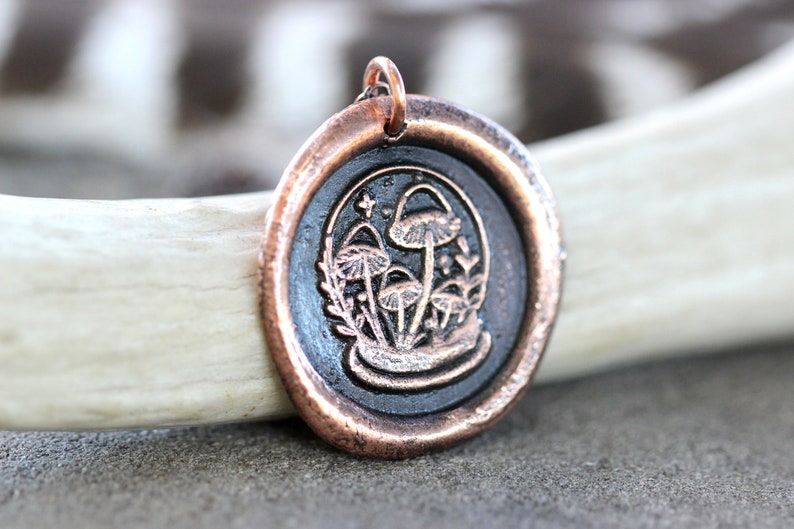 May include: A copper pendant with a black wax seal featuring a detailed illustration of mushrooms and foliage.