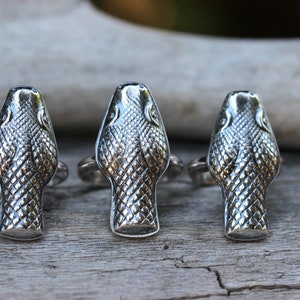 May include: Three silver rings featuring snake head designs. The snake heads are detailed with scales and have a textured finish.