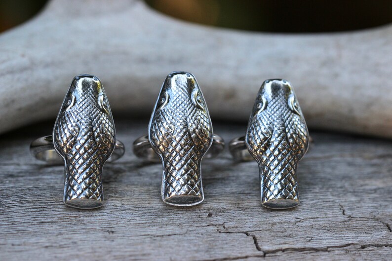 May include: Three silver rings featuring snake head designs. The snake heads are detailed with scales and have a textured finish.