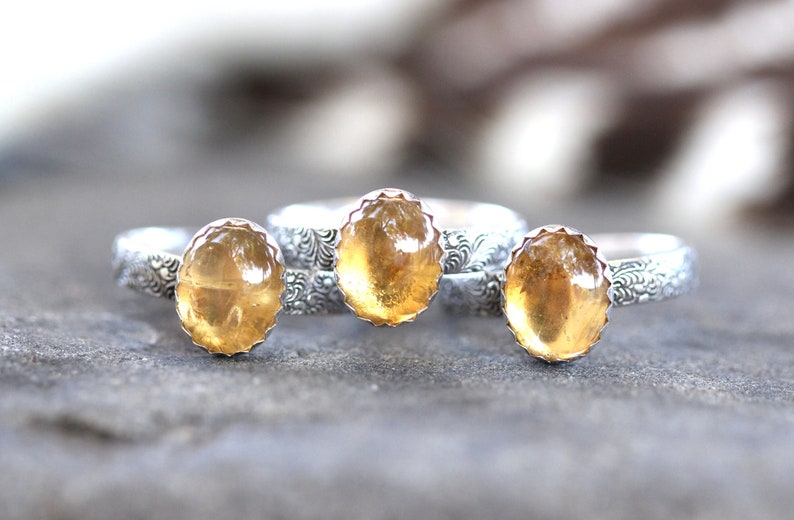 May include: Three silver rings with yellow gemstone settings. The rings have a decorative floral pattern.