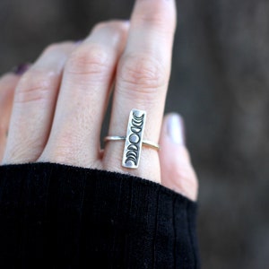 May include: A silver ring with a vertical design of eight crescent moons. The ring is worn on a person's finger.