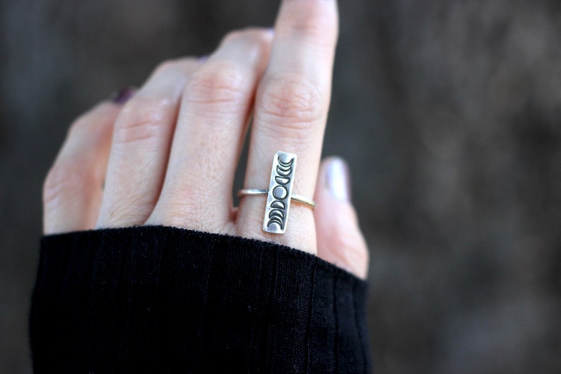 May include: A silver ring with a vertical design of eight crescent moons. The ring is worn on a person's finger.