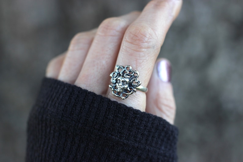 Puede incluir: Anillo de plata con un dise&ntilde;o detallado de una cara de mujer rodeada de serpientes.