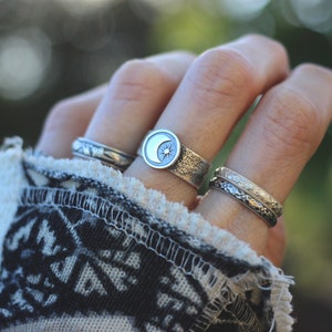 May include: A hand wearing three silver rings. The middle ring features a crescent moon with a star design. The other two rings are plain bands.