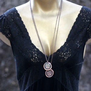 May include: A black lace top with a silver chain necklace featuring two round pendants. The pendants have a copper finish and a design of a tree with leaves.