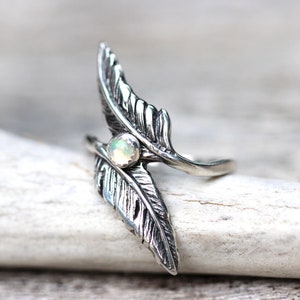 May include: A silver ring with two feather designs and a white opal gemstone in the center.