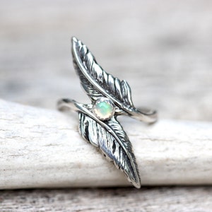 May include: A silver ring with two feather designs and a white opal gemstone in the center.