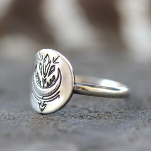 May include: A silver ring with a crescent moon design featuring a crystal and floral accents.