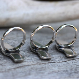 May include: Three silver rings with a unique design. The rings are stacked on top of each other and are in focus. The background is out of focus.