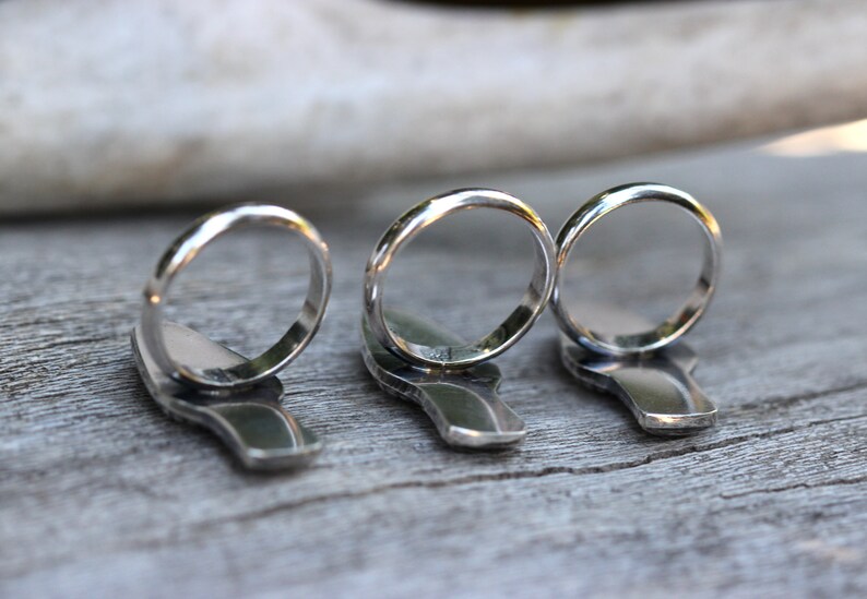 May include: Three silver rings with a unique design. The rings are stacked on top of each other and are in focus. The background is out of focus.