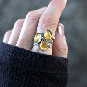 May include: Three silver rings with yellow oval gemstones. The rings are stacked on a finger.
