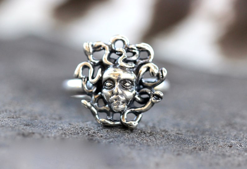 Puede incluir: Un anillo de plata con un dise&ntilde;o detallado de la cara de Medusa rodeada de serpientes.