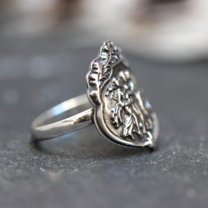 Puede incluir: Un anillo de plata con un dise&ntilde;o detallado y ornamentado que presenta un motivo floral. El anillo tiene forma de l&aacute;grima y una banda lisa.