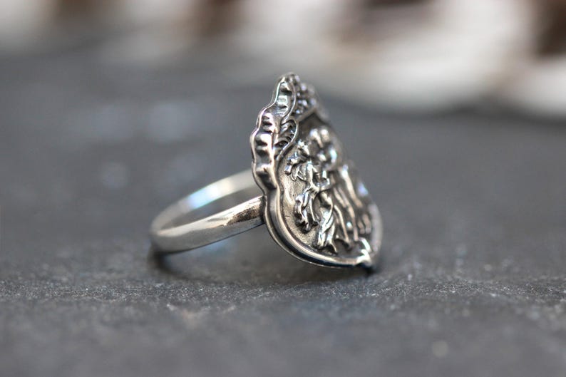 Puede incluir: Un anillo de plata con un dise&ntilde;o detallado y ornamentado que presenta un motivo floral. El anillo tiene forma de l&aacute;grima y una banda lisa.