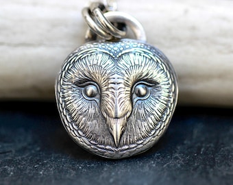 May include: A detailed silver pendant in the shape of an owl's face. The pendant features intricate detailing of the owl's feathers, eyes, and beak. The pendant is attached to a silver chain loop.