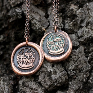 May include: Two copper necklaces with mushroom pendants. The pendants are round and have a green enamel background with a design of mushrooms and leaves. The chains are silver.