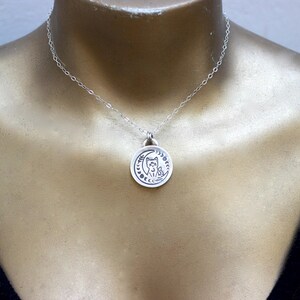 May include: A silver necklace with a pendant featuring a cat sitting on a crescent moon. The pendant is detailed with stars and other celestial symbols.