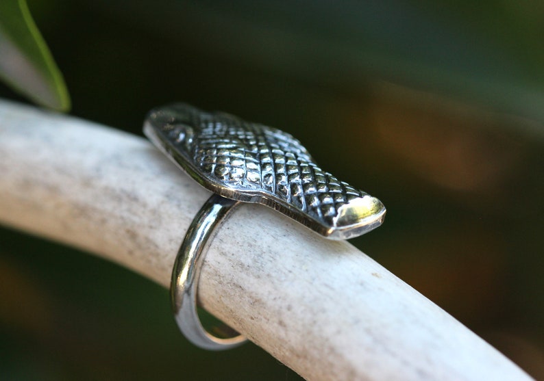 May include: A silver ring featuring a detailed alligator head design. The ring is displayed on a white background.