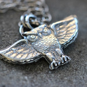 May include: Silver owl pendant with detailed wings and eyes. The owl is perched with its wings spread out.