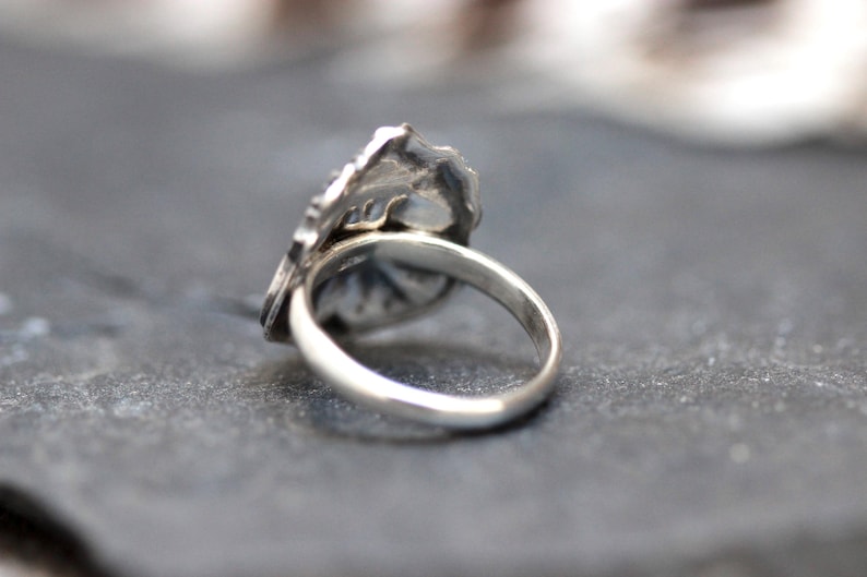 Puede incluir: Un anillo de plata con un dise&ntilde;o detallado en la parte superior. El anillo est&aacute; sobre una superficie gris.
