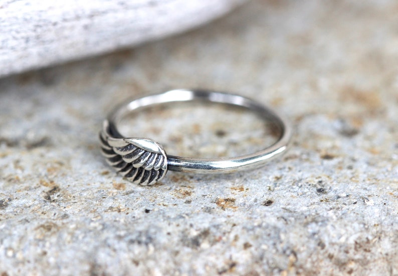 May include: A silver ring with a wing design. The wing is detailed with multiple lines to create a realistic look.