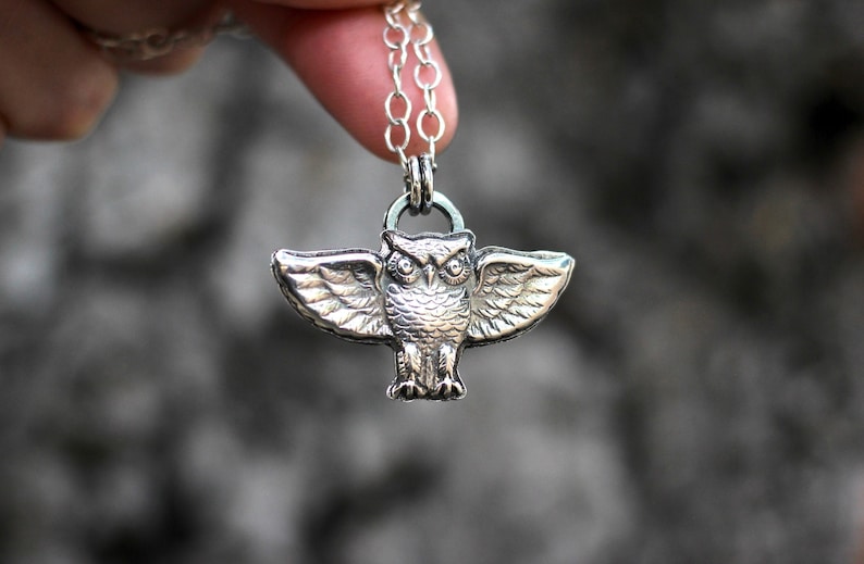 May include: Silver owl pendant necklace with a detailed design. The owl is perched with its wings spread out.